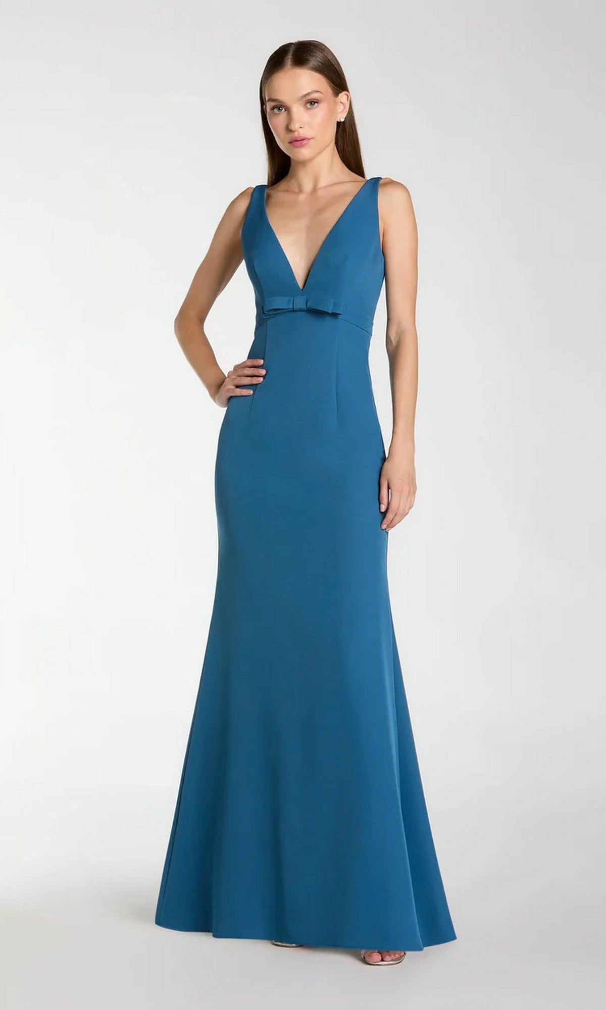 A woman models the Mac Duggal 2371, a sleeveless teal floor-length formal crepe dress with a deep V-neck and small waist bow, standing against a plain light background.